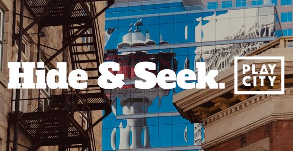 Hide & Seek. PlayCity logo. Behind text is a window reflection of the Calgary Tower.